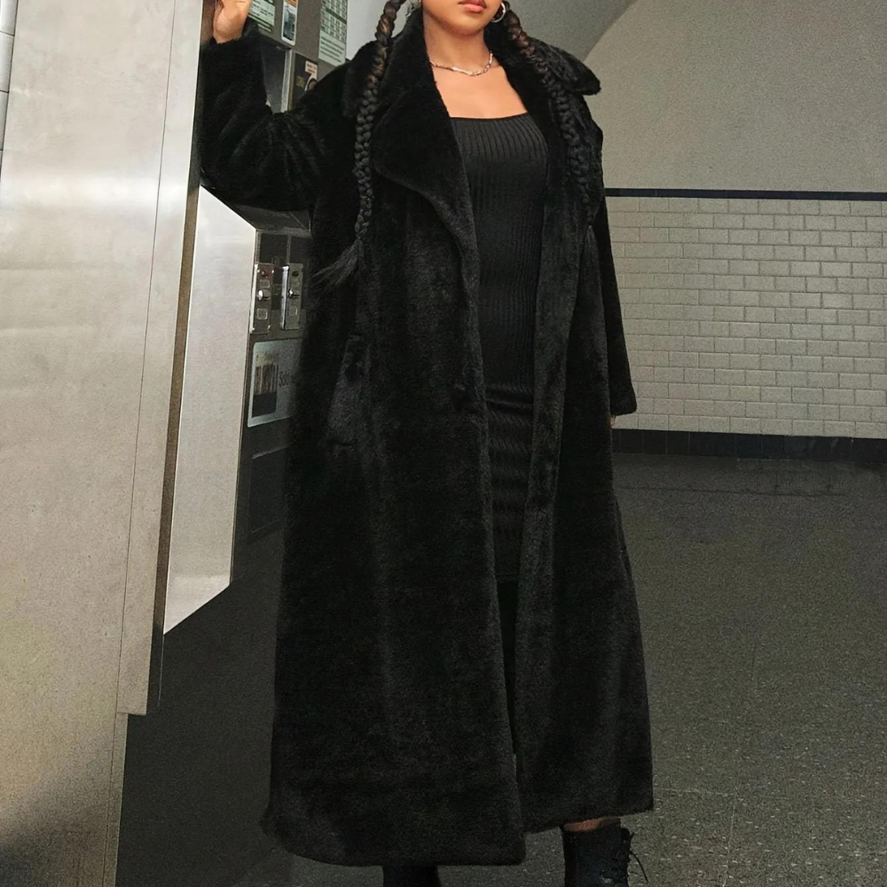 Zwarte lange faux fur jas, gedragen door vrouw met vlechten, in metrostation. Stijlvolle wintermode, elegant en warm, perfect voor koude dagen.