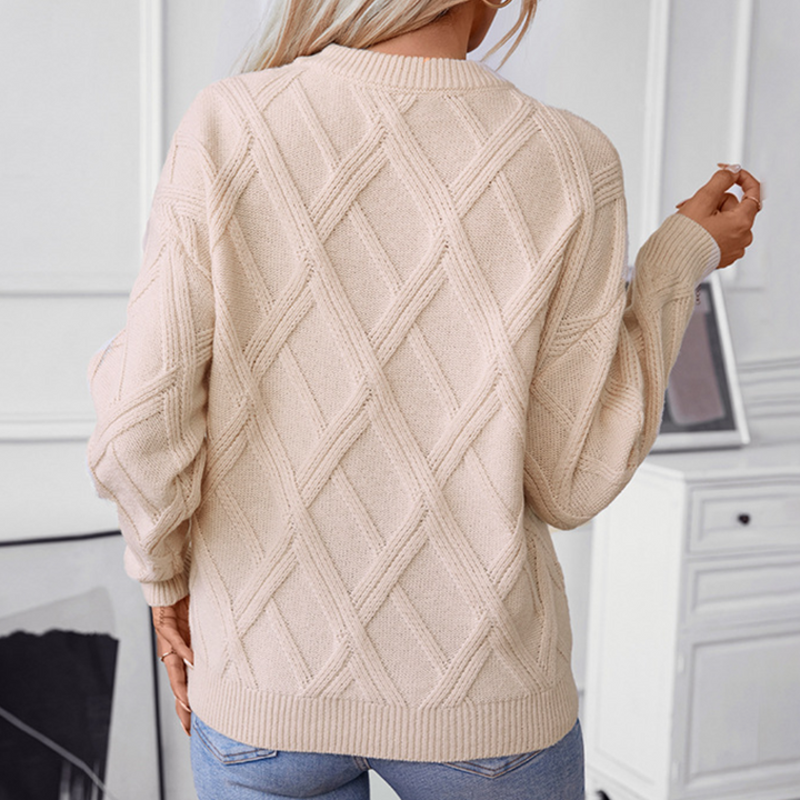 Beige gebreide trui met ruitpatroon, gedragen door een persoon, tegen een lichte achtergrond. Modieuze dameskleding, herfst-winter stijl.