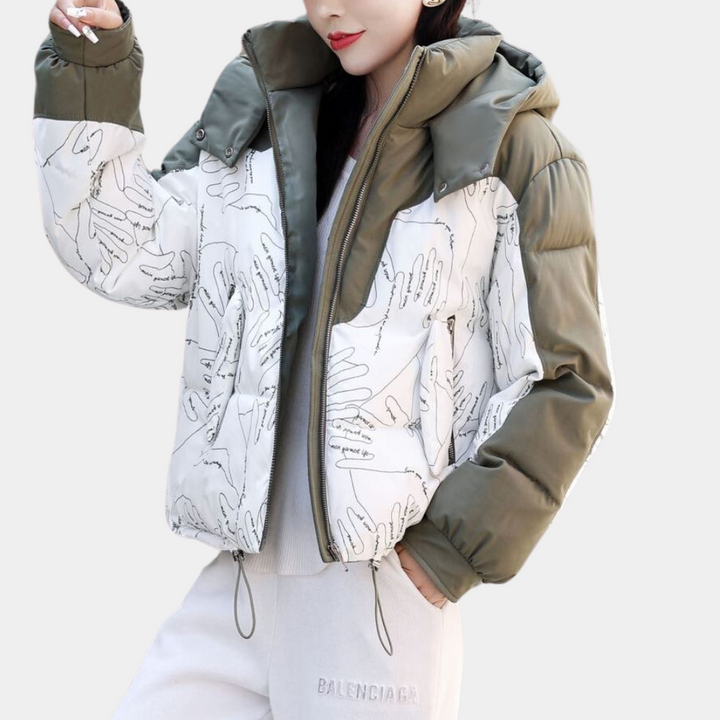 Vrouw in stijlvolle winterjas met handafdrukken, olijfgroene mouwen en capuchon, gecombineerd met grijze joggingbroek. Trendy wintermode.