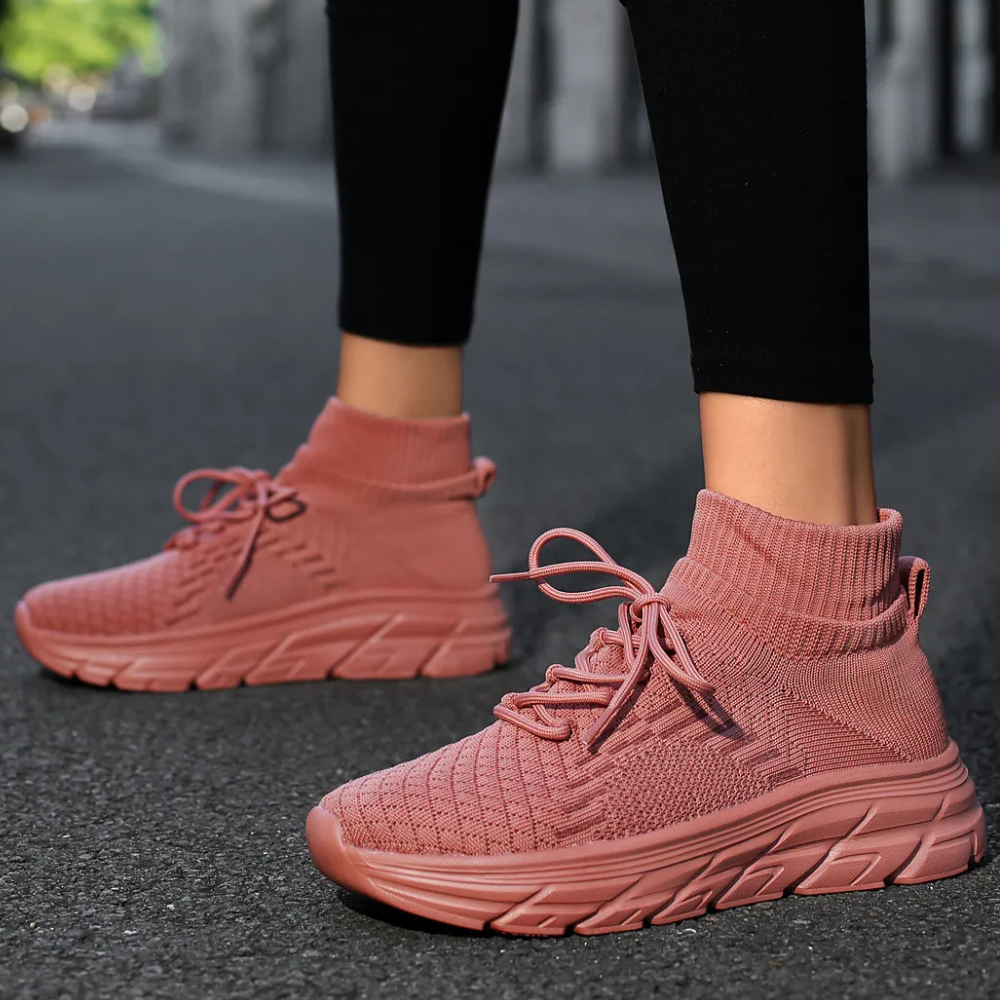 Roze gebreide sneakers met hoge sokkraag, comfortabele zool en veters, gedragen door persoon op stoep. Trendy damesmode, casual schoenen.