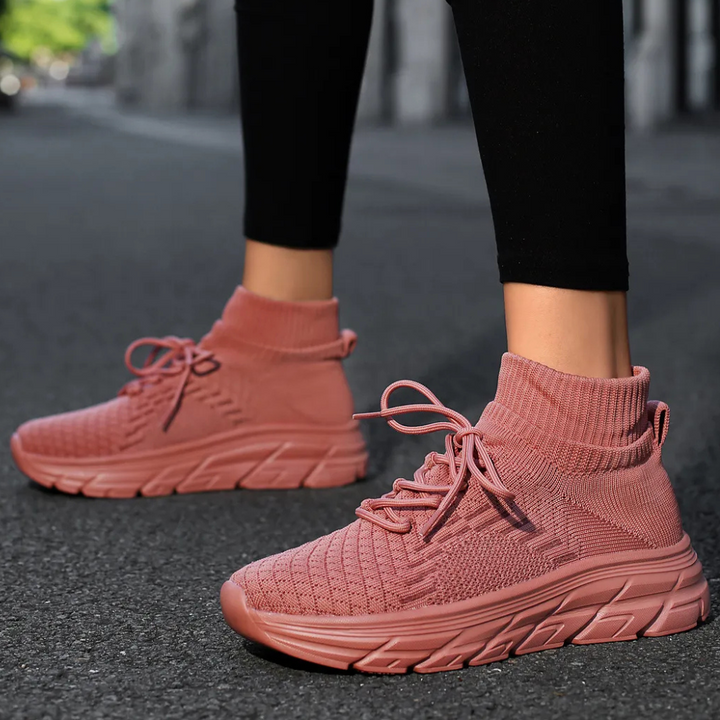 Roze gebreide sneakers met hoge sokkraag, comfortabele zool en veters, gedragen door persoon op stoep. Trendy damesmode, casual schoenen.