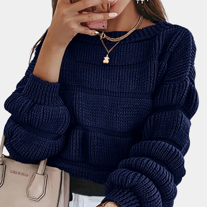 Vrouw met donkerblauwe gebreide trui, gouden ketting en beige handtas. Modieuze herfstkleding, trendy damesmode, casual stijl.