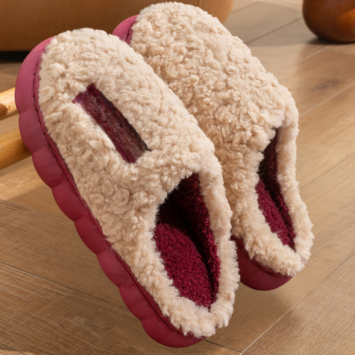 Beige pluche pantoffels met bordeauxrode voering op houten vloer. Warme winterpantoffels, comfortabel en stijlvol voor thuisgebruik.