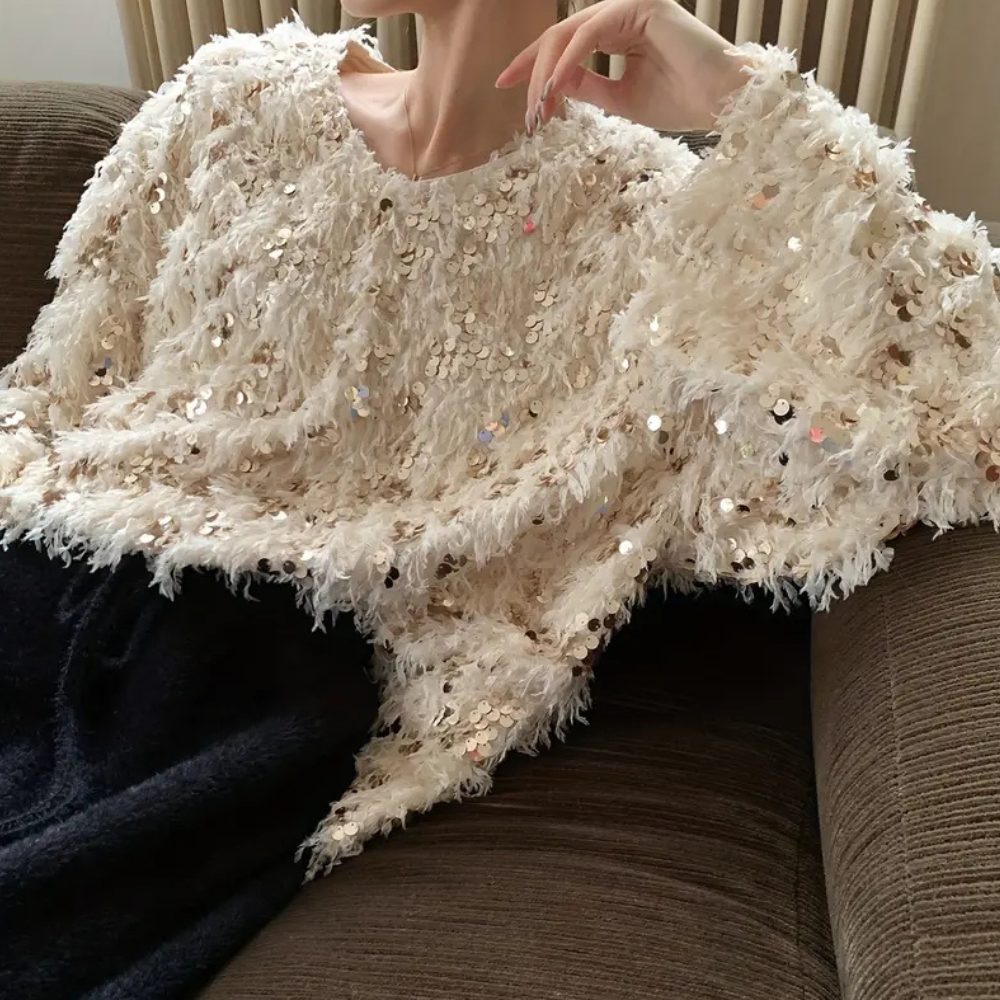 Vrouw in beige pailletten trui, zittend op een bruine bank. Modieuze, glinsterende kleding, perfect voor feestelijke gelegenheden.