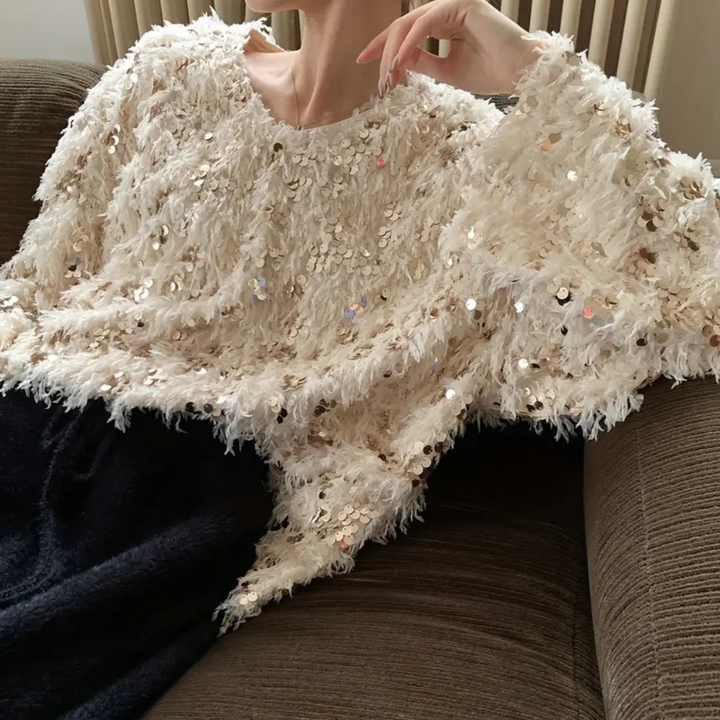 Vrouw in beige pailletten trui, zittend op een bruine bank. Modieuze, glinsterende kleding, perfect voor feestelijke gelegenheden.