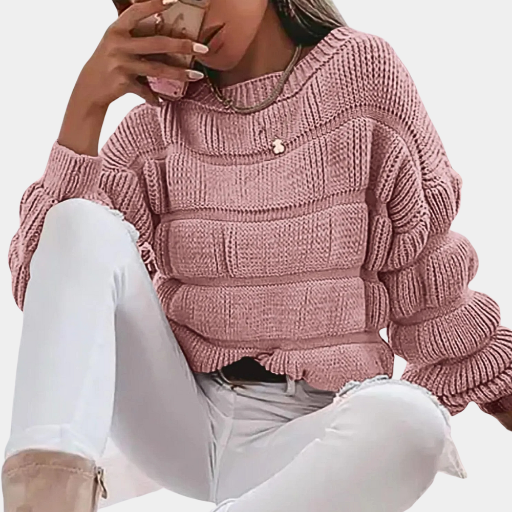 Vrouw in roze gebreide trui met geribbelde textuur, zittend in witte broek. Modieuze dameskleding, herfst-winter stijl, casual outfit.