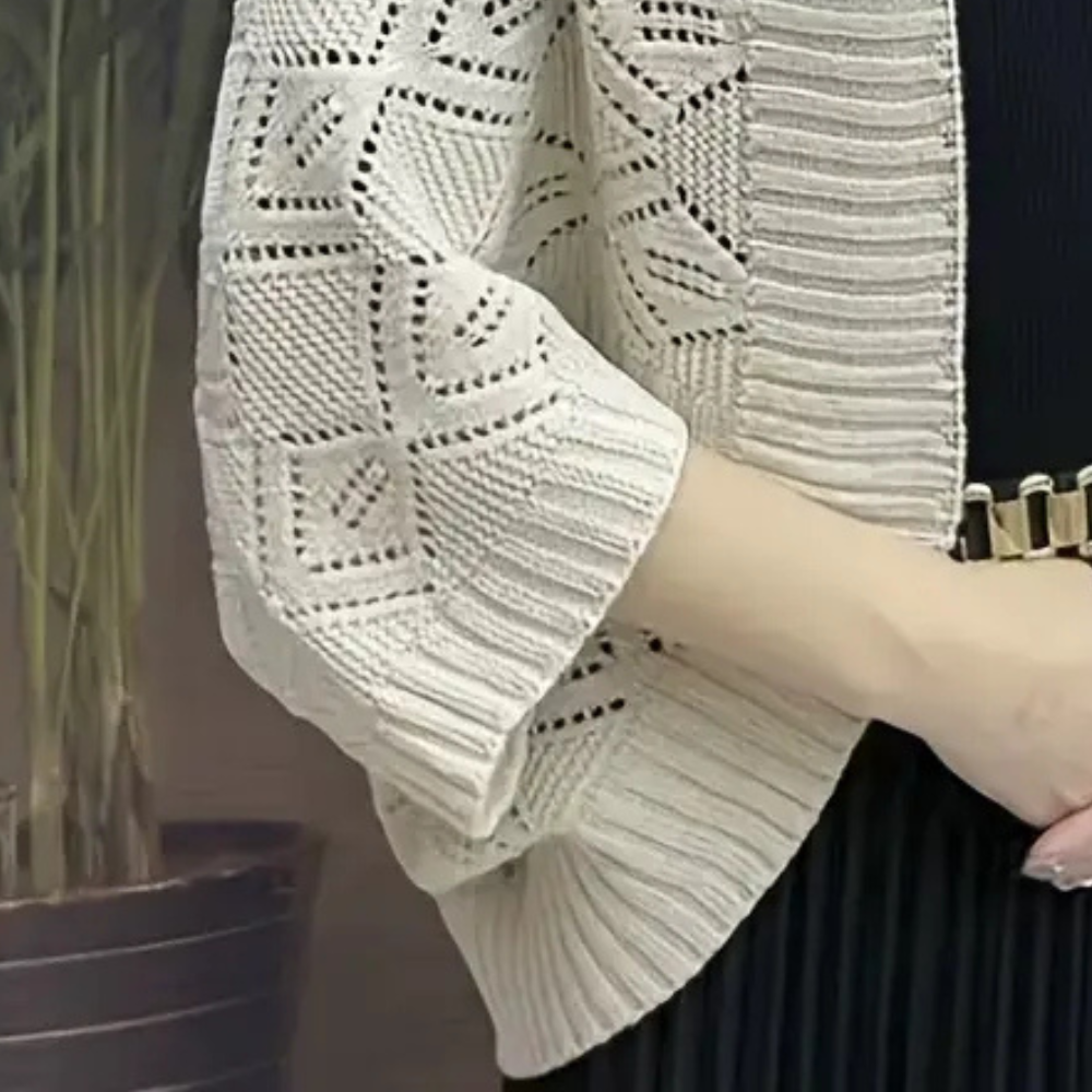 Beige gebreid vest met opengewerkt patroon, gedragen door persoon in zwarte jurk. Stijlvol en elegant, perfect voor casual en formele gelegenheden.