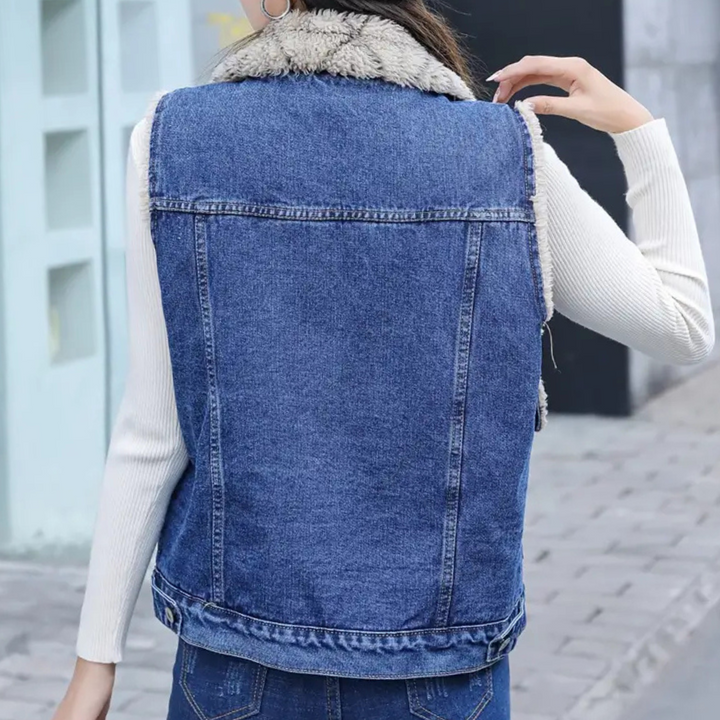 Vrouw in blauwe spijkerjas met schapenvachtkraag, witte trui eronder, staand op een stoep. Modieuze winterkleding, casual stijl.