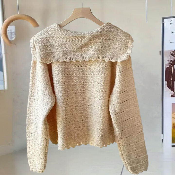Beige gehaakte trui op houten hanger, gedetailleerd patroon, lange mouwen, modieuze dameskleding, boho-stijl, interieur achtergrond.