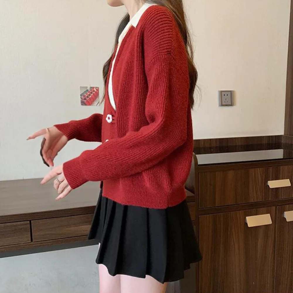 Vrouw in rode gebreide trui en zwarte rok, staand bij houten kast. Modieuze dameskleding, herfstoutfit, casual stijl.