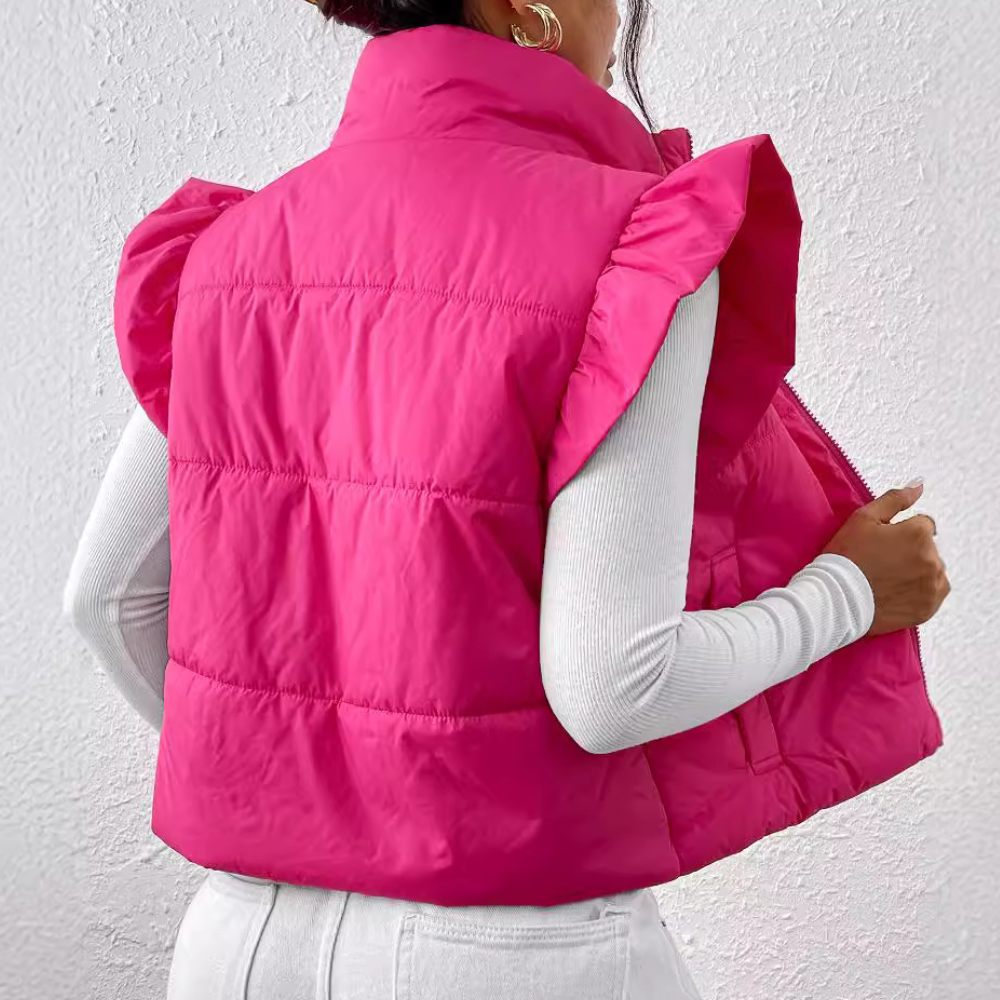 Vrouw draagt felroze gewatteerd vest met ruches, gecombineerd met witte trui en broek. Modieuze dameskleding, trendy winteroutfit.