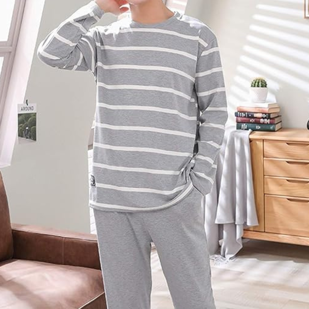 Man in grijs-wit gestreepte pyjama in moderne woonkamer, ontspannen pose. Comfortabele loungewear, casual mode, huiselijke sfeer.