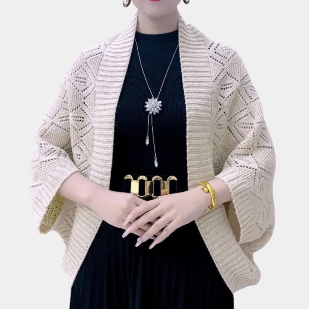 Vrouw draagt gebreid beige vest met diamantpatroon, zwarte jurk, gouden riem en sieraden. Modieuze dameskleding, herfststijl, elegant design.