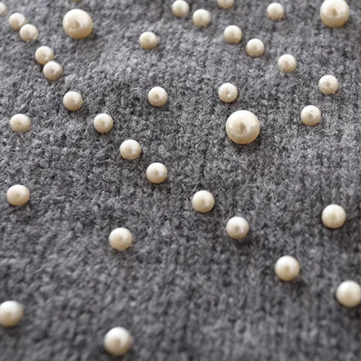 Grijze gebreide stof met decoratieve parels, close-up. Modieuze textieltrend, elegante parelversiering, stijlvolle kledingdetails.
