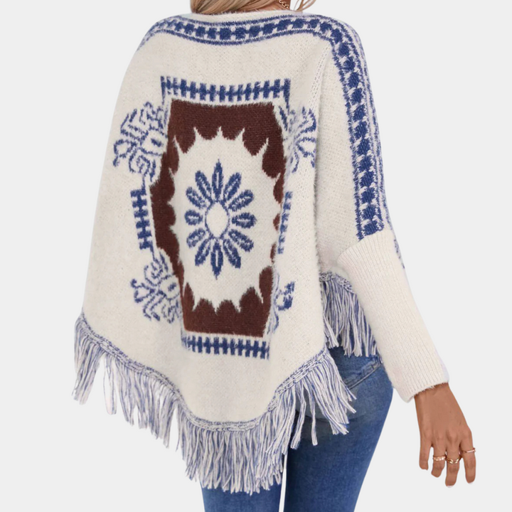 Vrouw draagt gebreide poncho met blauwe en bruine bloemenprint en franjes, casual mode, herfstkleding, bohemian stijl, comfortabele dameskleding.