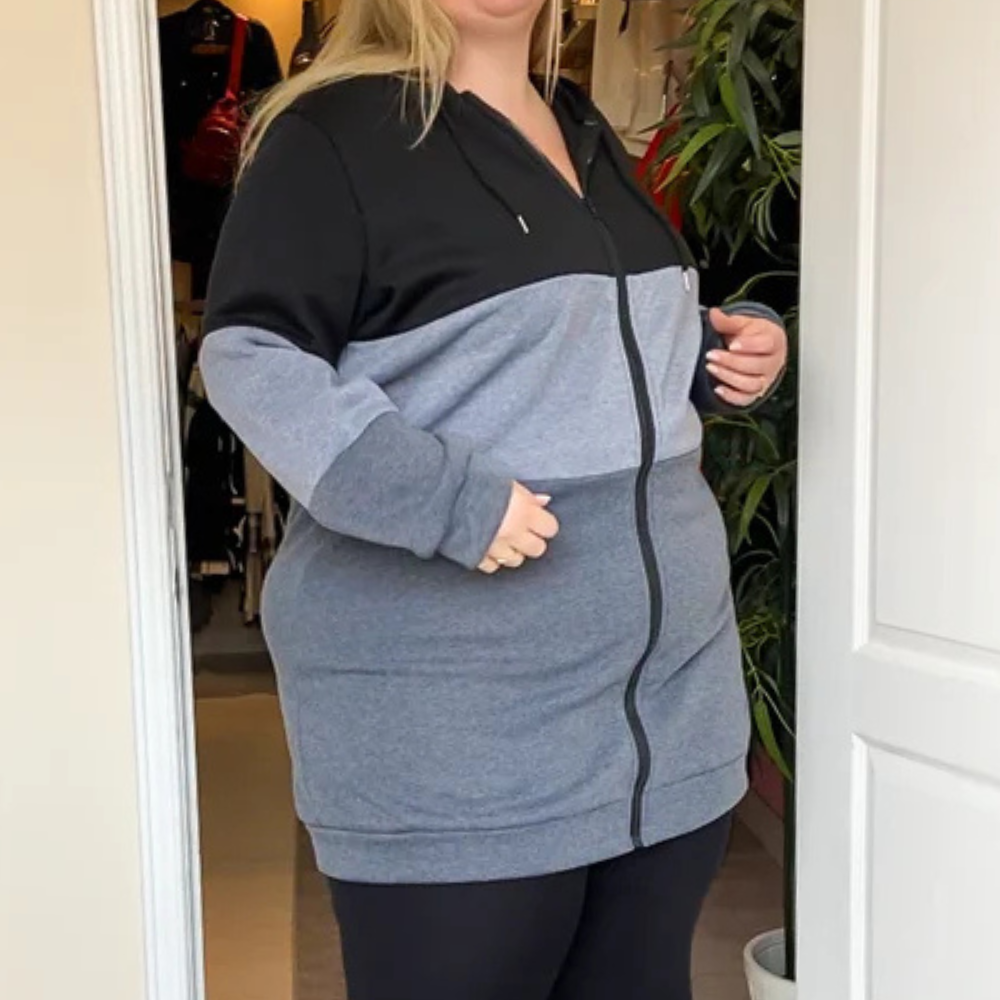 Vrouw in comfortabele, tweekleurige hoodie met rits, zwart en grijs, bij deuropening. Casual mode, plus-size kleding, herfststijl.