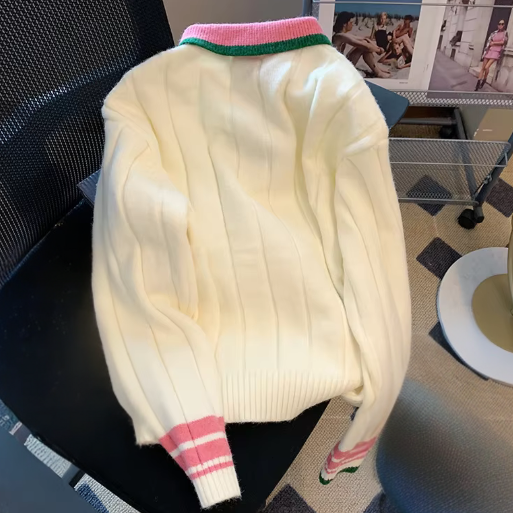 Crèmekleurige trui met roze en groene accenten, geribbelde boorden, op een zwarte stoel. Perfect voor herfstmode en casual outfits.