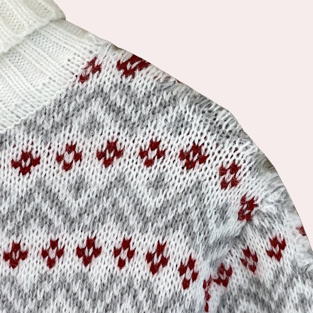 Wit en grijs gebreide trui met rood zigzagpatroon, close-up. Warme winterkleding, Scandinavisch design, zachte wolmix.
