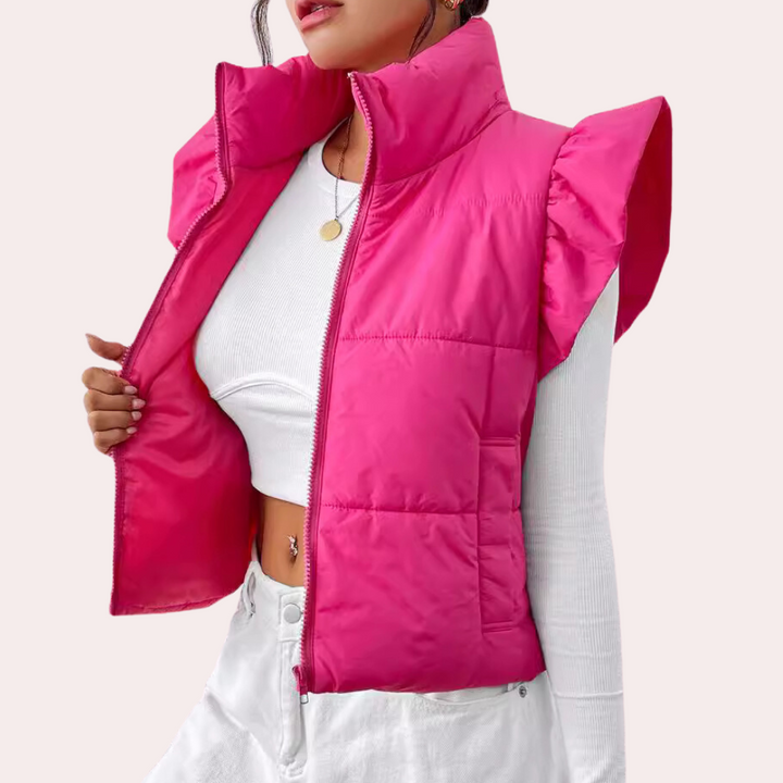 Roze gewatteerd damesvest met opstaande kraag en ruches, gedragen over een witte crop top en broek. Modieuze winterkleding, trendy stijl.