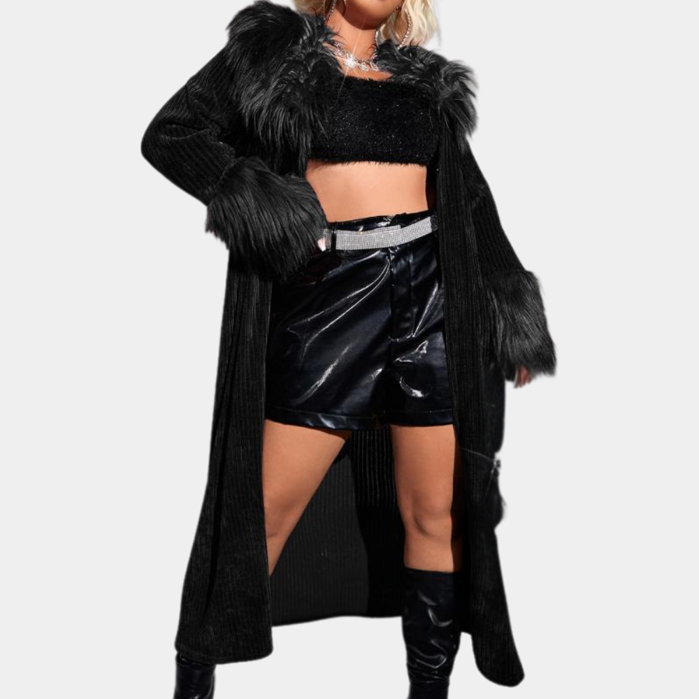 Zwarte lange jas met nepbontkraag en -manchetten, gecombineerd met glanzende zwarte shorts en een crop top. Trendy damesmode, winteroutfit.