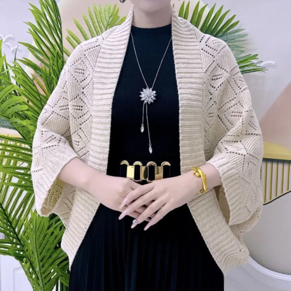 Vrouw in zwarte jurk met beige gebreid vest, gouden riem en sieraden, voor groene planten. Modieuze dameskleding, herfststijl.