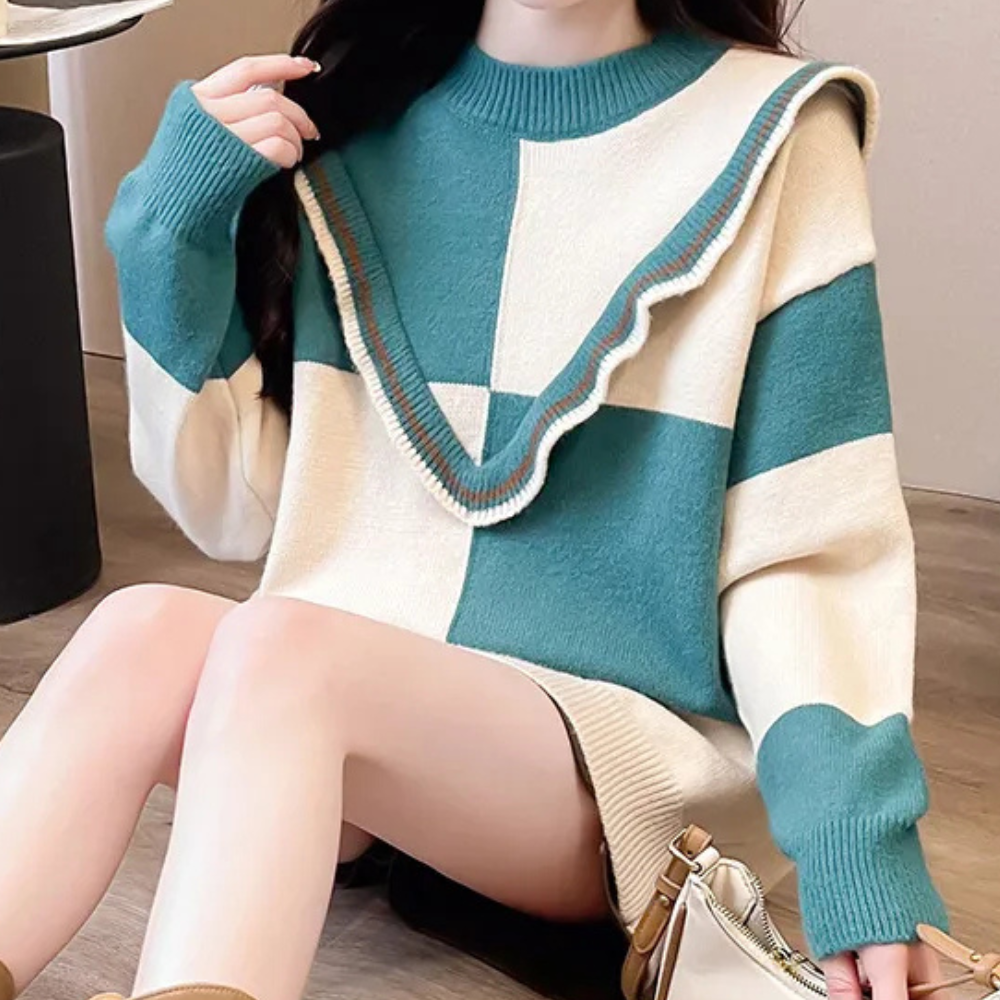 Vrouw draagt oversized gebreide trui met blauw-witte blokken en geribbelde kraag. Trendy wintermode, comfortabele dameskleding, casual stijl.