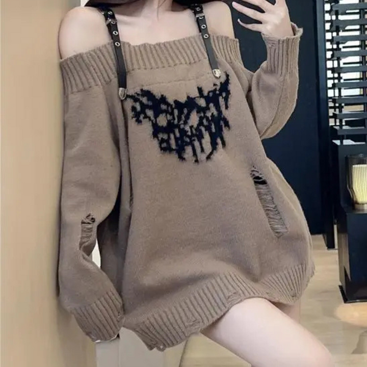 Vrouw draagt oversized bruine trui met schouderbanden en zwarte print, modieuze streetwear, trendy herfstkleding, comfortabele casual stijl.