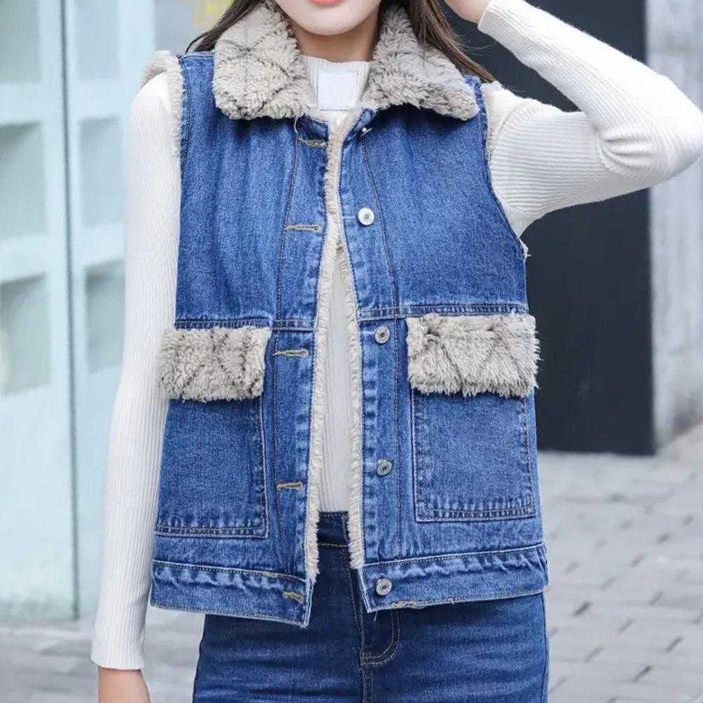 Vrouw draagt blauwe spijkerjas met schapenvacht kraag en zakken, witte trui eronder. Modieuze winterkleding, casual straatstijl.