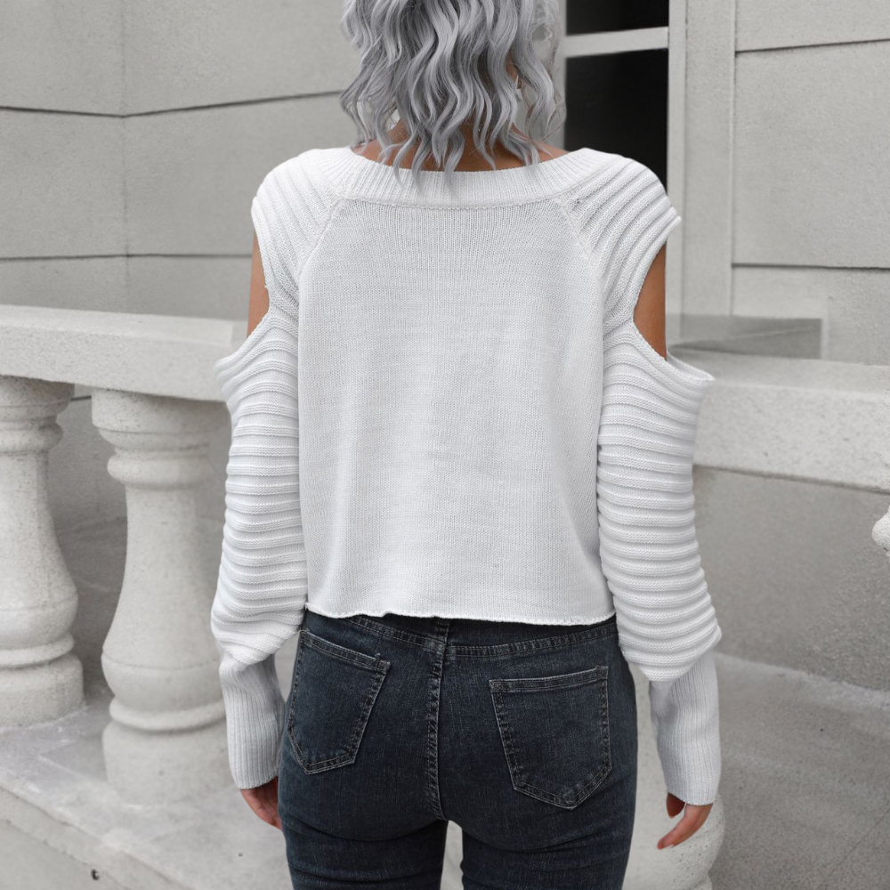 Vrouw in witte open schoudertrui en donkere jeans, rugaanzicht, grijze krullende haren, stedelijke achtergrond. Modieuze dameskleding, herfststijl.