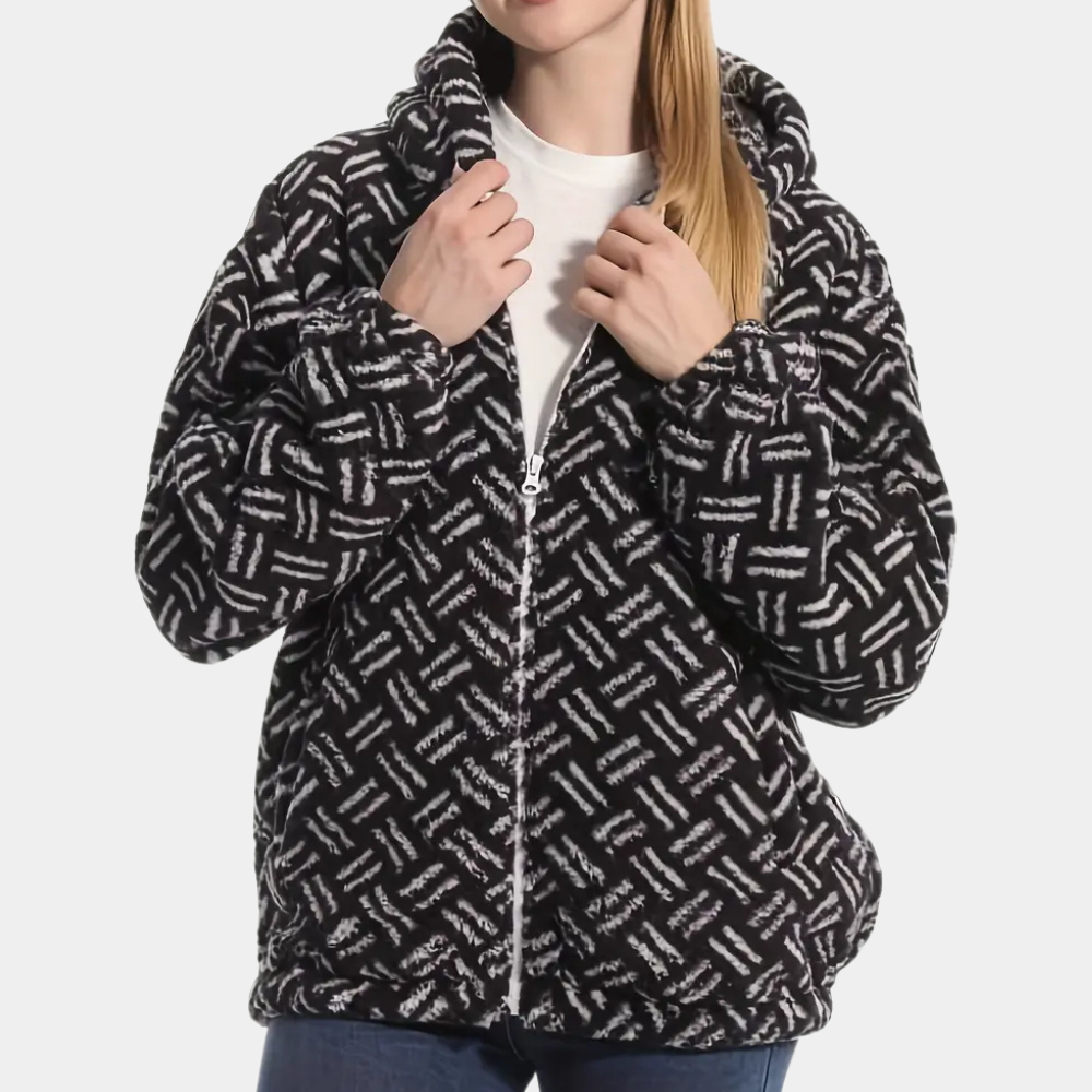 Vrouw draagt zwarte fleece hoodie met wit geometrisch patroon, ritssluiting en capuchon. Comfortabele winterkleding, trendy damesmode.