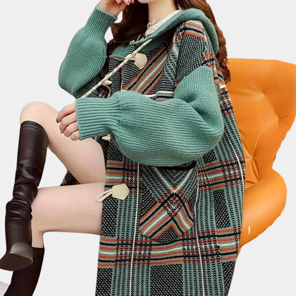 Groene geruite oversized trui met capuchon en knopen, gedragen door zittende vrouw op oranje stoel. Modieuze dameskleding, herfst-winter stijl.