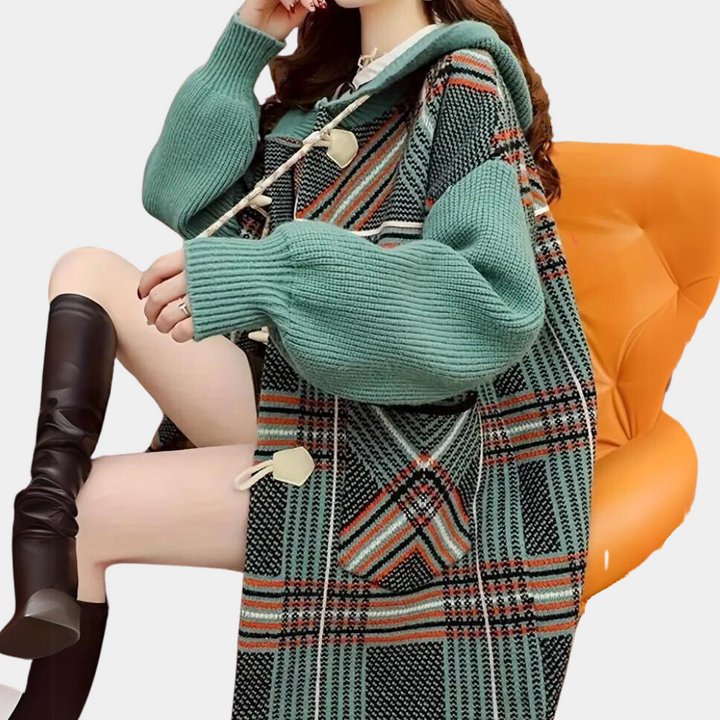 Groene geruite oversized trui met capuchon en knopen, gedragen door zittende vrouw op oranje stoel. Modieuze dameskleding, herfst-winter stijl.