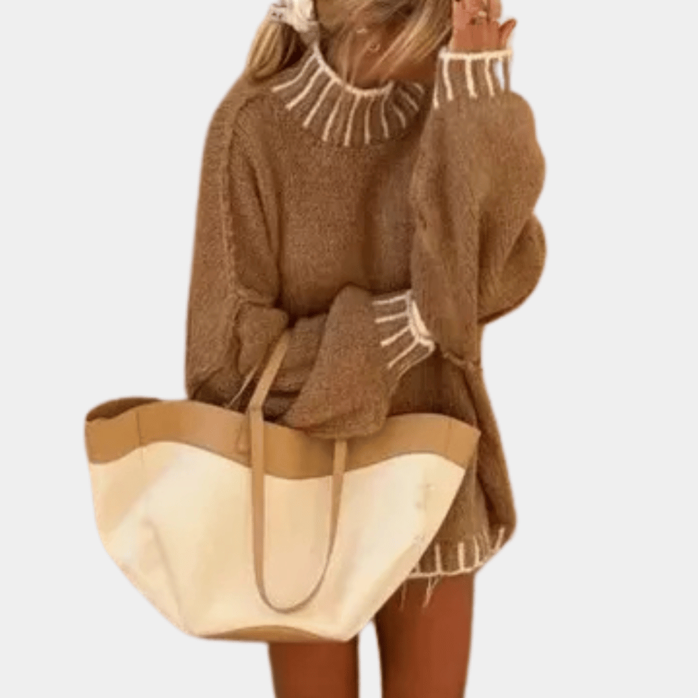 Vrouw in oversized bruine trui met witte accenten, draagt een grote beige en witte tas. Modieuze herfstoutfit, casual dameskleding.