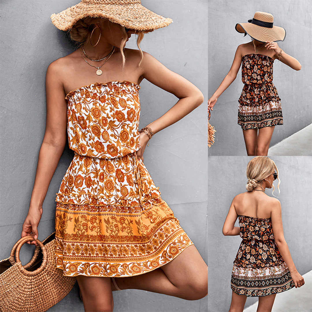 Vrouw in zomerse boho-jurk met bloemenprint en strohoed, poseert tegen grijze muur. Trendy damesmode, casual zomeroutfit, bohemian stijl.