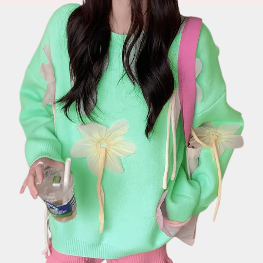 Vrouw in mintgroene trui met bloemenprint, draagt roze tas en houdt een plastic beker vast. Trendy damesmode, casual outfit, kleurrijke kleding.
