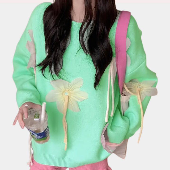 Vrouw in mintgroene trui met bloemenprint, draagt roze tas en houdt een plastic beker vast. Trendy damesmode, casual outfit, kleurrijke kleding.