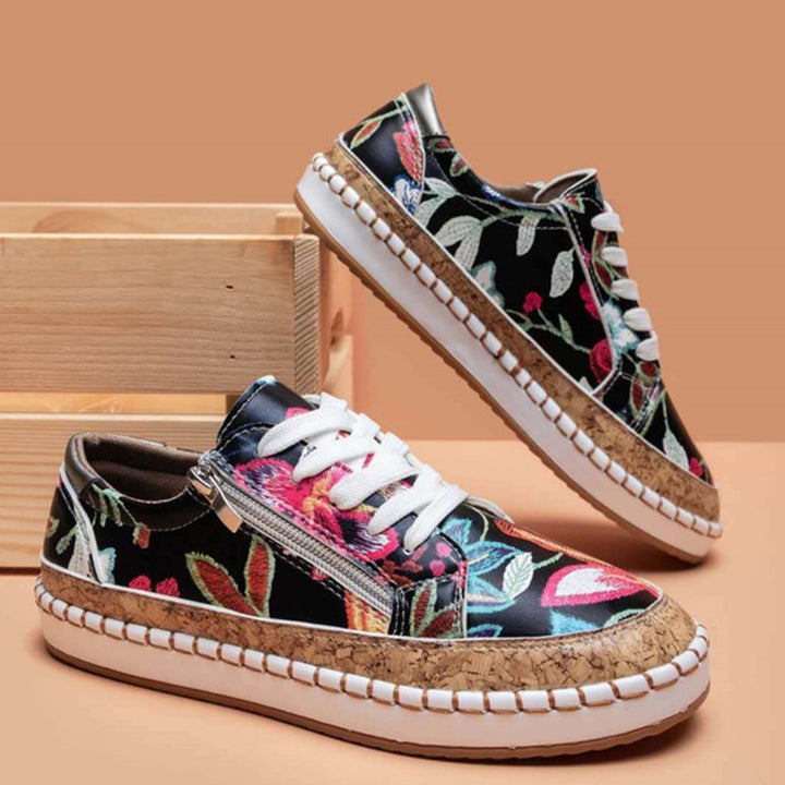 Zwarte sneakers met kleurrijke bloemenprint, witte veters en kurkzool, naast houten kist. Trendy damesschoenen, casual stijl.