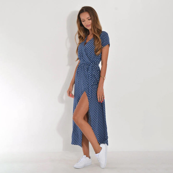 Vrouw in blauwe polkadot jurk met split, witte sneakers, tegen witte achtergrond. Mode, zomerjurk, casual stijl.