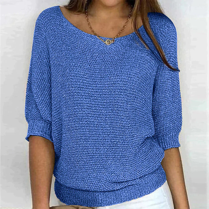 Vrouw in blauwe gebreide trui met driekwart mouwen, ronde hals en witte broek. Modieuze dameskleding, casual stijl, comfortabele pasvorm.