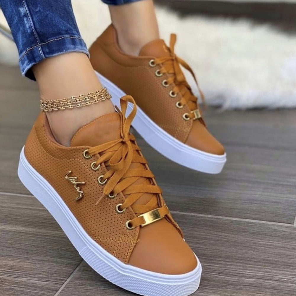 Bruine leren sneakers met witte zolen en gouden details, gedragen door een persoon op een houten vloer. Stijlvolle casual schoenen voor dames.