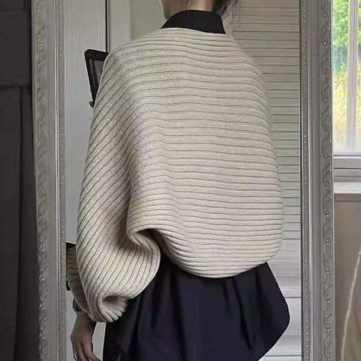 Vrouw in moderne, oversized gebreide trui met ribbelpatroon, zwarte kraag, voor spiegel. Stijlvolle herfstmode, minimalistisch design, trendy outfit.