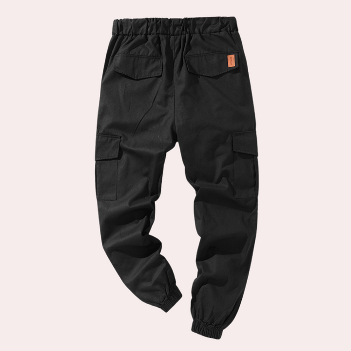 Zwarte cargobroek met elastische tailleband, meerdere zakken en een oranje label. Ideaal voor casual en outdoor activiteiten. Unisex design.