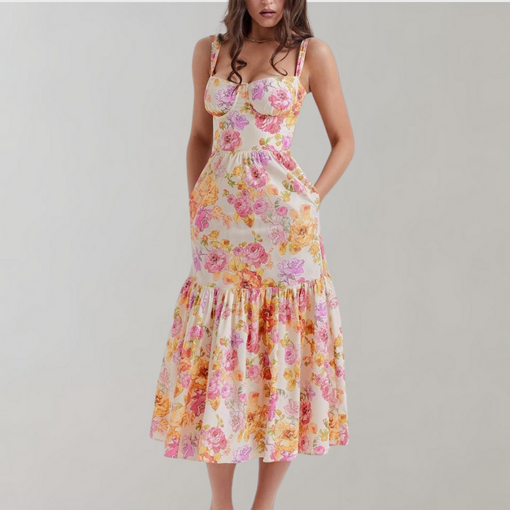 Vrouw in bloemenjurk met roze en gele bloemenprint, mouwloos ontwerp, midi-lengte, zomermode, elegante casual stijl.