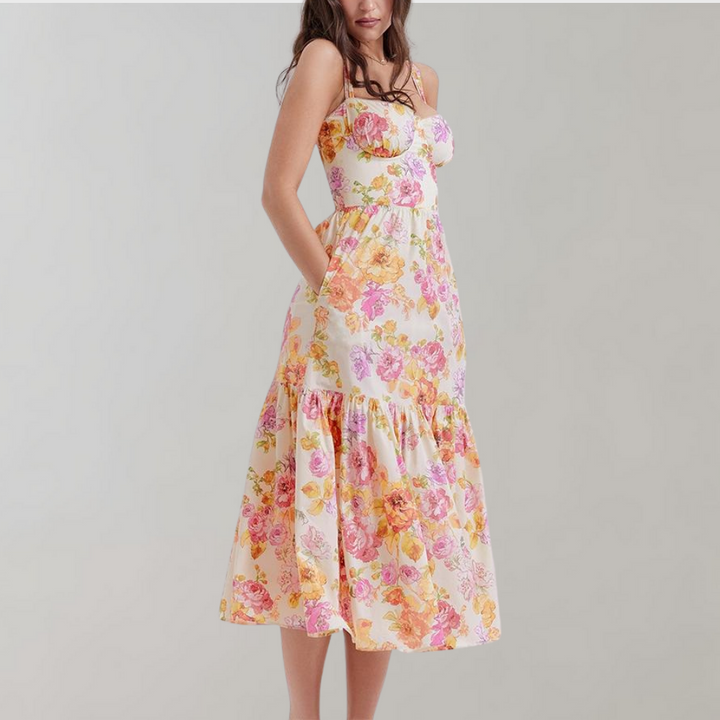 Vrouw in bloemenjurk met roze en gele bloemenprint, mouwloos en met ruches, tegen een neutrale achtergrond. Zomermode, dameskleding, casual stijl.
