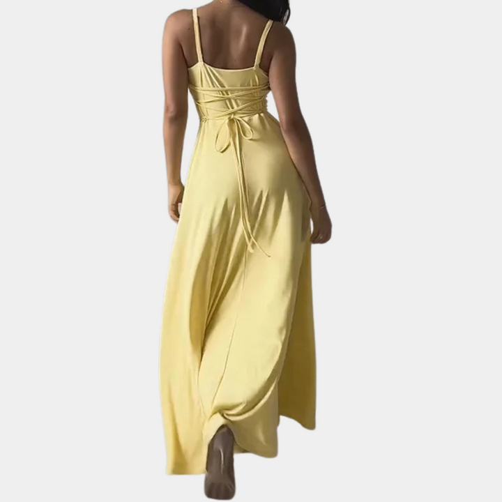 Vrouw in lange gele zomerjurk met rugbanden, elegante avondjurk, modieuze dameskleding, perfect voor zomerse gelegenheden.