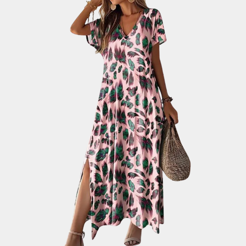 Vrouw in roze maxi-jurk met groene bladprint, korte mouwen en V-hals, draagt een rieten tas. Perfect voor zomermode en casual stijl.