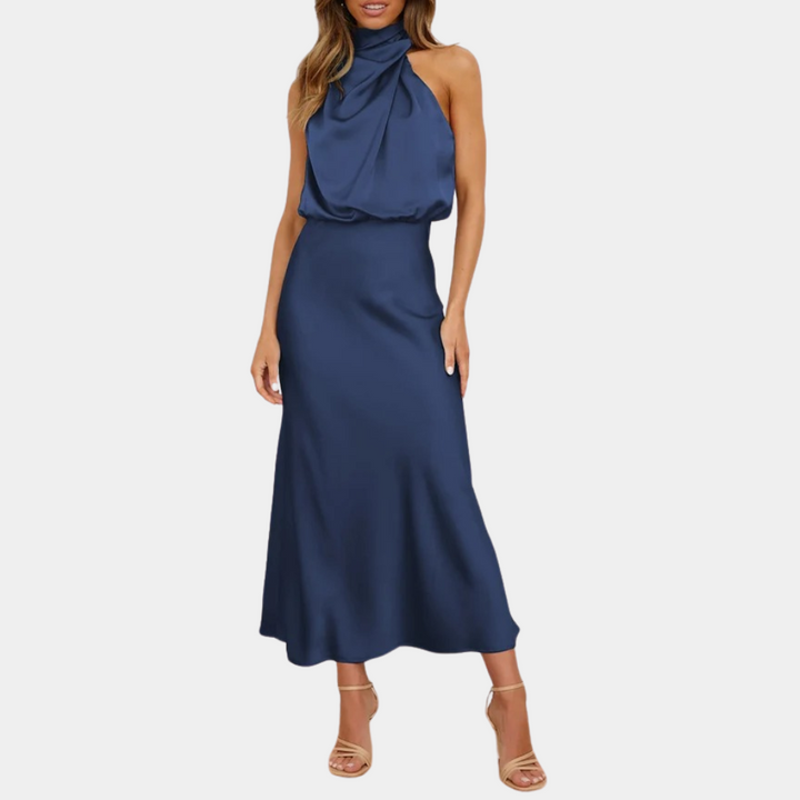 Vrouw in elegante, mouwloze, marineblauwe satijnen jurk met halternek, staand op witte achtergrond. Perfect voor avondkleding en formele evenementen.