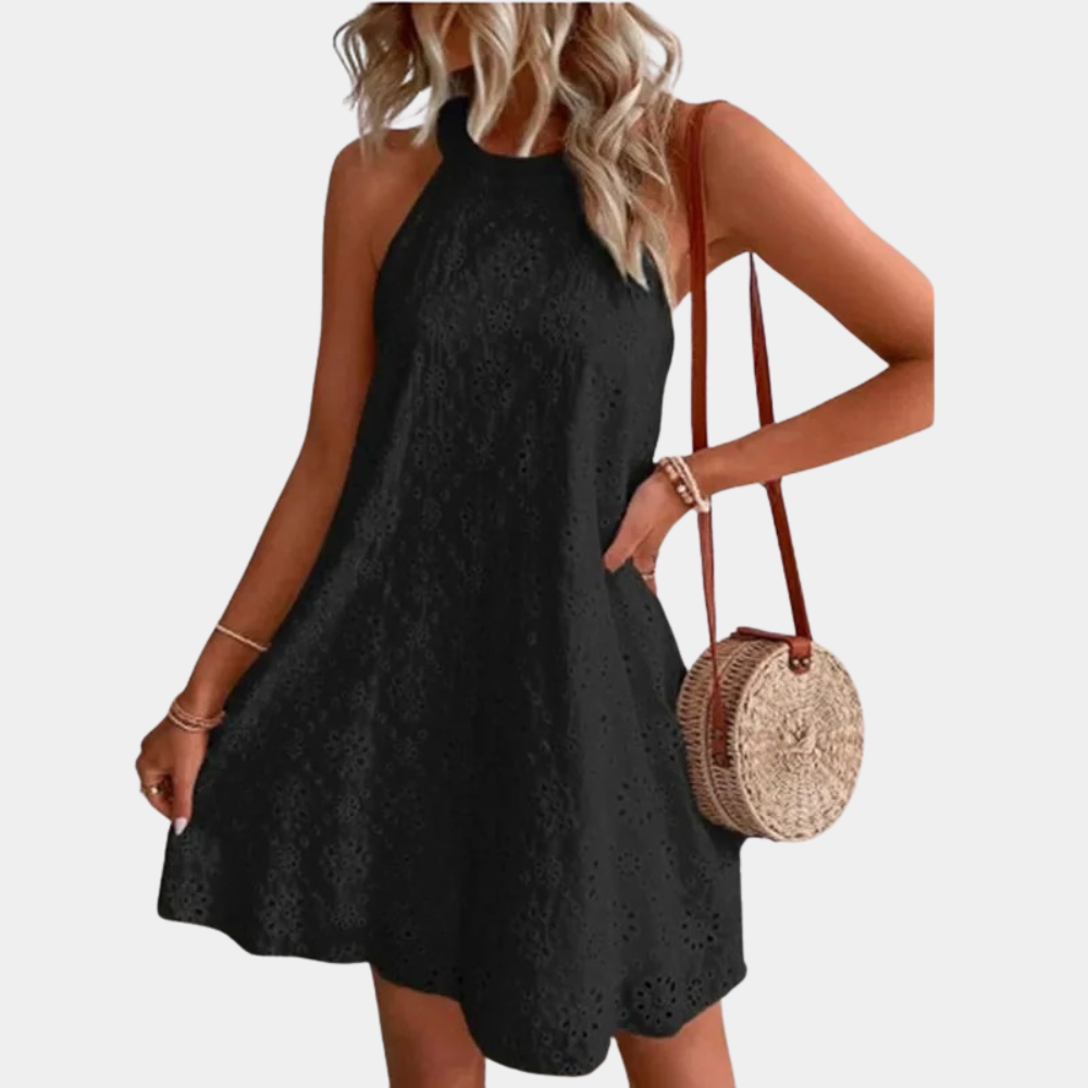 Zwarte mouwloze jurk met halternek, gedragen door vrouw met blond haar. Rieten ronde tas als accessoire. Perfect voor zomerse mode en casual stijl.
