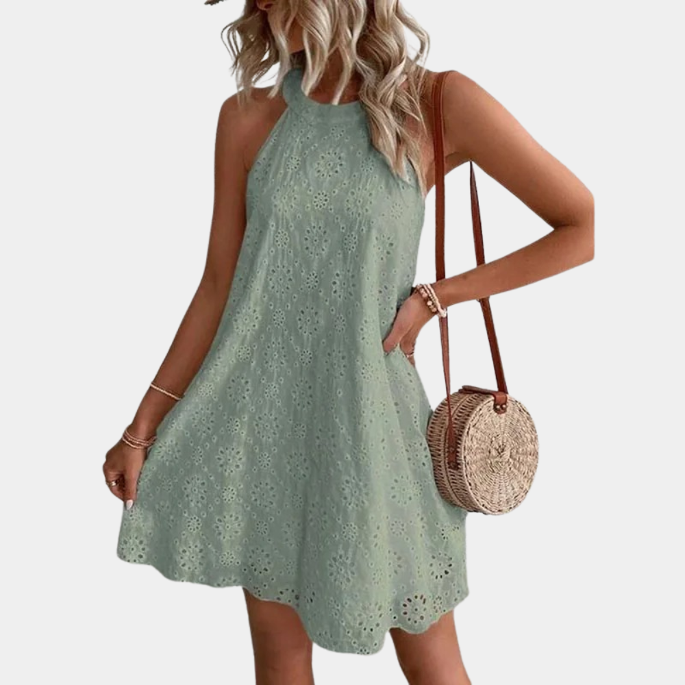 Vrouw in groene zomerjurk met broderie, halternek en ronde rieten tas. Perfect voor casual zomermode en stranduitjes.