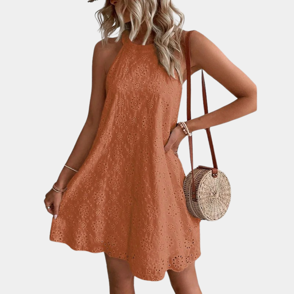 Oranje zomerjurk met bloemenpatroon, mouwloos en halternek. Vrouw draagt een ronde rieten tas. Perfect voor casual zomermode.